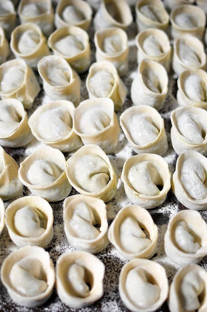 Stos surowych domowych pierogów Tortellini Pelmeni Uszka z mąką gotową do gotowania s