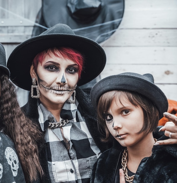 Straszny rodzinny matek córki świętujące Halloween Przerażający czarny makijaż półtwarzy czaszki i kostiumy czarownicy stylowe obrazyHorrorfun na imprezie dla dzieci w stodole na ulicyCzapkiKurtki