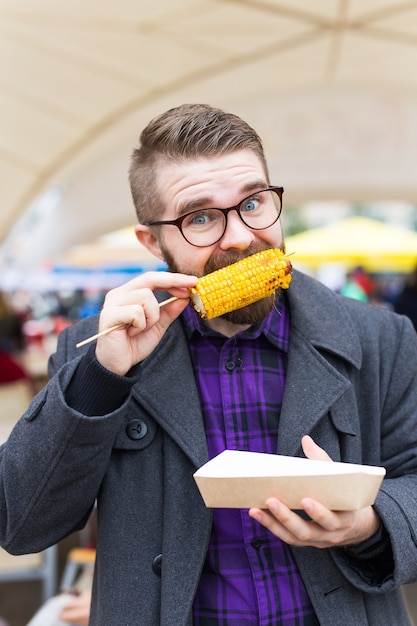 Street Food I Kuchnia Koncepcja - Człowiek Jedzenie Kukurydzy Z Grilla. Jedzenie Wegetariańskie. Zdrowe I Smaczne Warzywa.