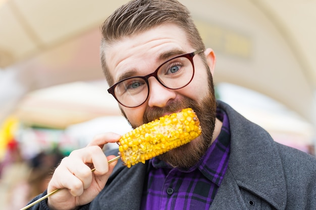 Zdjęcie street food i kuchnia koncepcja - człowiek jedzenie kukurydzy z grilla. jedzenie wegetariańskie. zdrowe i smaczne warzywa.