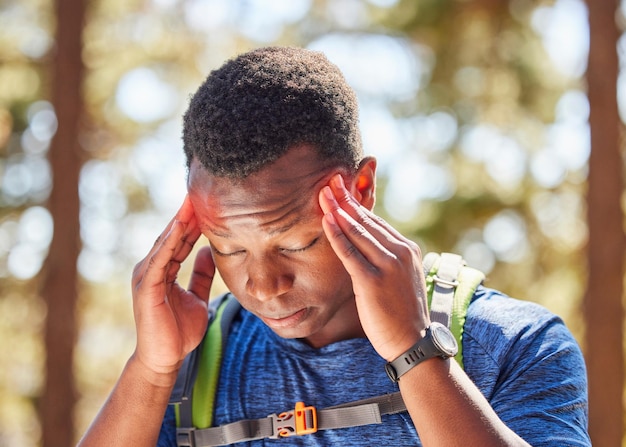 Stres wędrujący z bólem głowy z czarnym sportowcem trzymającym bolące skronie podczas spaceru po lesie Przyrodniczy fitness i migrena z męskim wycieczkowiczem w lesie do ćwiczeń lub treningu