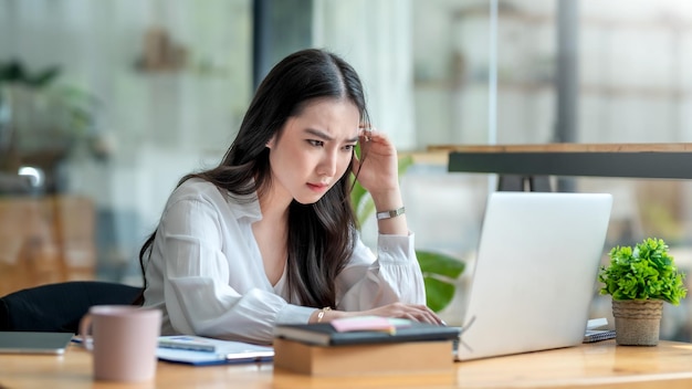 Stresujący dzień. Młoda azjatycka bizneswoman podkreślił podczas pracy na laptopie w biurze.