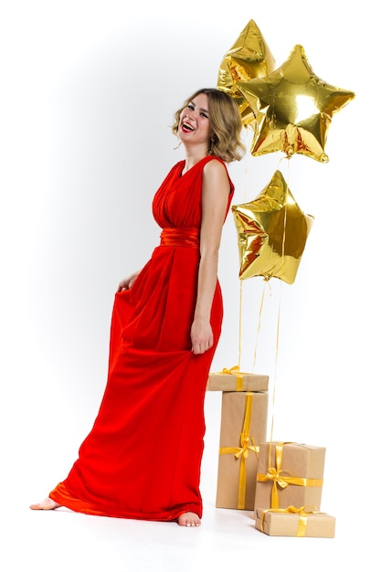 Strona zdjęcie elegancji seksowna pani w czerwonej sukience z czerwonymi ustami i blond piękne kręcone włosy, uśmiechając się. Tło złote balony i prezenty. Koncepcja sprzedaży
