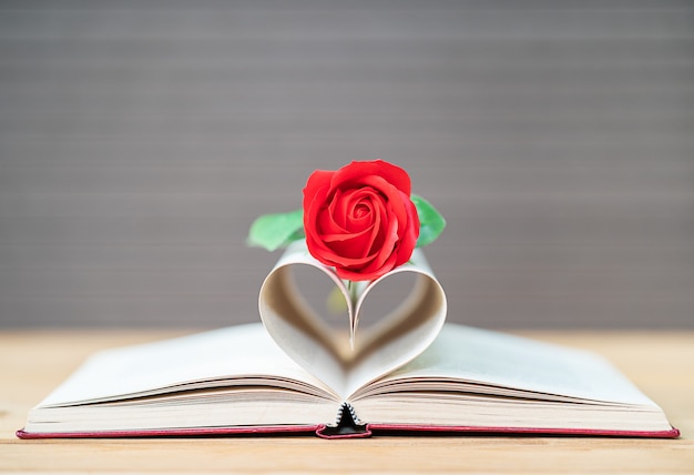 Strony książki o zakrzywionym kształcie serca i czerwonej róży