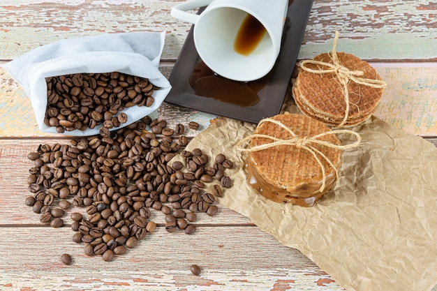 Stroopwafle ułożone na brązowym papierze, obok leżącej filiżanki z kawą (widok z góry).