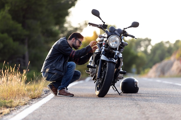 Strzał młody człowiek rowerzysta sprawdzania jego motocykl przed jazdą na drodze.