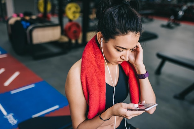 Strzał z góry portret pięknej sportowej młodej kobiety słuchającej muzyki ze swojego smartfona po przerwie po treningu na siłowni Ludzie technologia fitness i koncepcja sportu