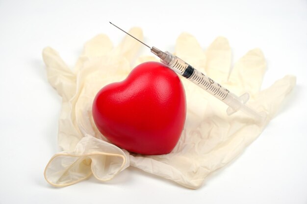 Strzykawka z czerwonym sercem i gumowe rękawiczki medyczne na białym tle z miejscem na kopię Koncepcja leczenia chorób serca