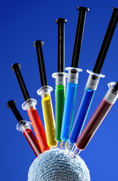 Zdjęcie strzykawki medyczne z wielokolorową zawartością utkwione w miękkiej kulce na niebieskim tle pomysł na zdrowy nastrój