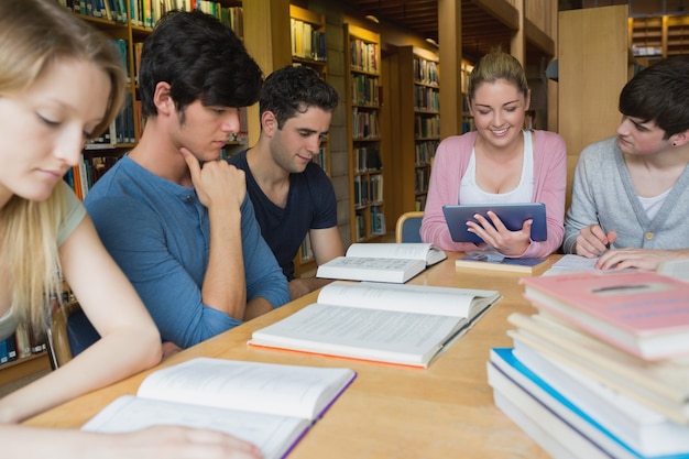 Studenci studiujący razem w bibliotece z jednym przy użyciu komputera typu tablet