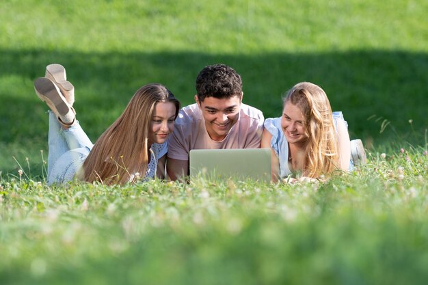 Studenci wieloetnicznych pracujący razem na laptopie leżącym na trawie
