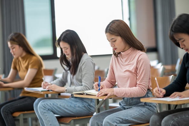 Studenci zdają egzaminy przy ławkach w klasie uniwersytetu.