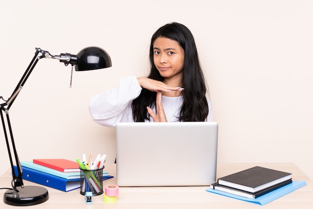 Studencka Azjatykcia Dziewczyna W Miejscu Pracy Z Laptopem Na Beż ścianie Robi Czasowi Out Gestykuluje