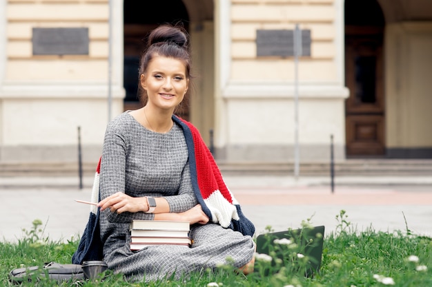 Studencka dziewczyna siedzi na trawie blisko książek uniwersyteckiego z książkami