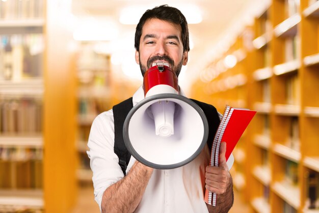 Studencki mężczyzna krzyczy megafonem na defocused bibliotece