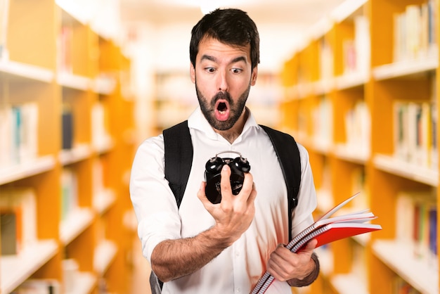 Studencki mężczyzna mienia rocznika zegar na defocused bibliotece