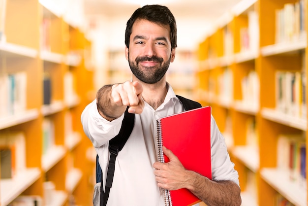 Studencki mężczyzna wskazuje przód na defocused bibliotece