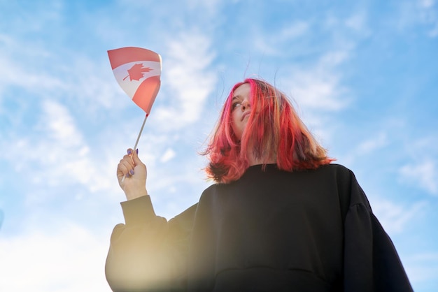 Student dziewczyna nastolatek z flagą Kanady w ręku, błękitne niebo z chmurami w tle. Kanada, edukacja i młodzież, koncepcja ludzi patriotyzmu