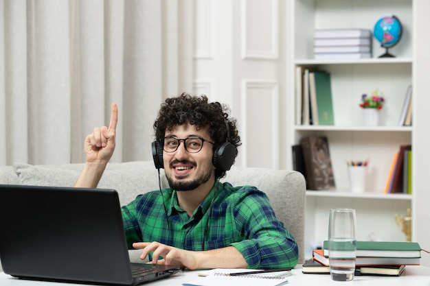 Student online ładny młody facet studiujący na komputerze w okularach w zielonej koszuli uśmiechnięty