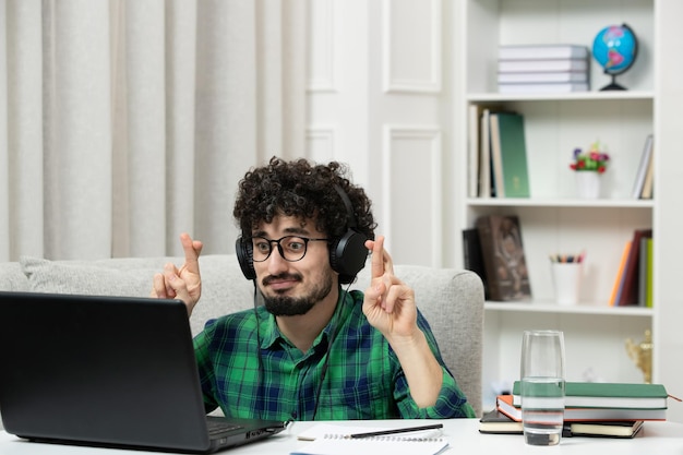 Student online ładny młody facet studiuje na komputerze w okularach w zielonej koszuli, krzyżując palce