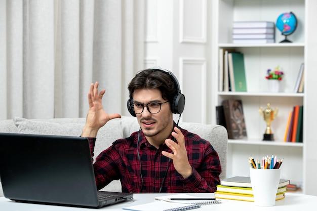 Student online młody facet w kraciastej koszuli w okularach studiuje na komputerze zirytowany i szalony