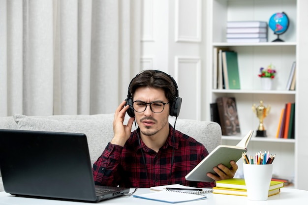 Student online, słodki facet w kraciastej koszuli i okularach, uczący się na komputerze, starając się pozostać skoncentrowanym