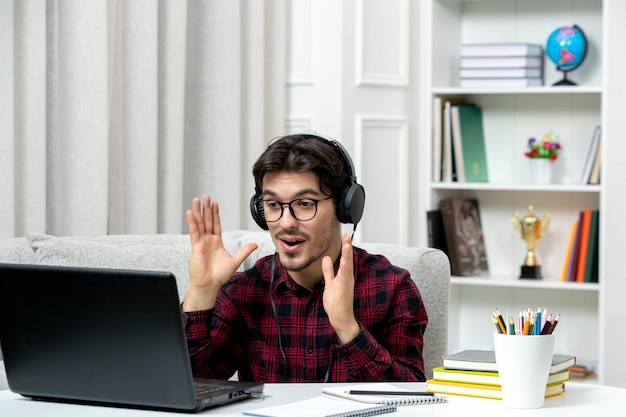 Student online słodki facet w kraciastej koszuli w okularach studiujący na komputerze machający radośnie rękami