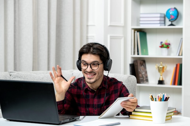 Student online słodki facet w kraciastej koszuli w okularach studiuje na komputerze machając i uśmiechając się