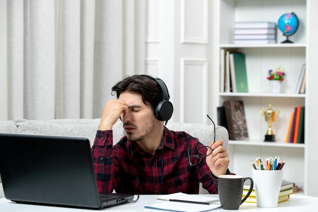 Student online słodki facet w kraciastej koszuli w okularach uczący się na komputerze zmęczony i wyczerpany