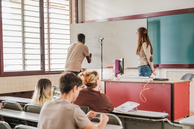 Student rozwiązuje zadanie na tablicy przed nauczycielem i kolegą z uczelni