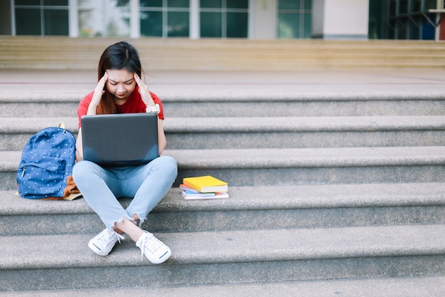 Student siedzi na schodach i pracy na wolnym powietrzu na laptopie na uniwersytecie.