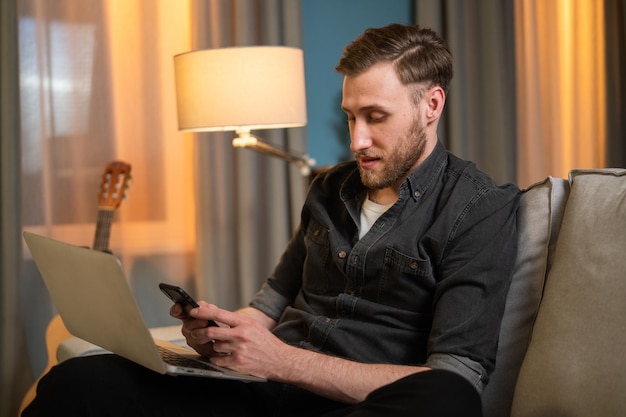 Student siedzi wieczorem na kanapie w salonie przed ekranem laptopa stojąc na kolanach