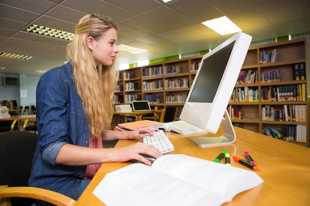 Student studiuje w bibliotece z komputerem