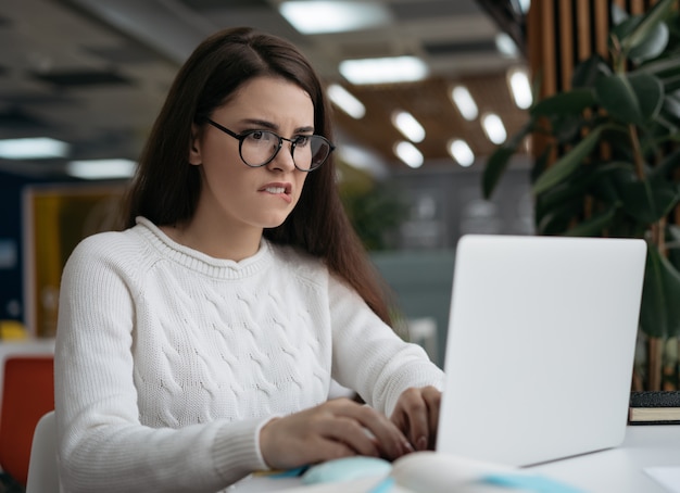 Student uniwersytetu korzysta z laptopa, studiuje online, przygotowuje się do egzaminu