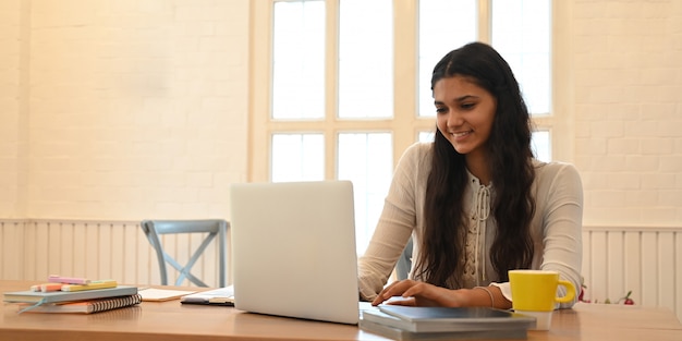 Student uniwersytetu uczy się lekcji online, siedząc przy drewnianym biurku.