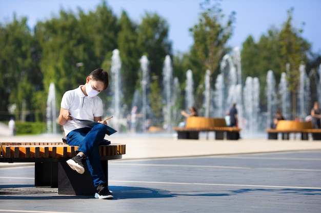 Student w masce odrabia lekcje na ulicznej ławce podczas pandemii COVID-19