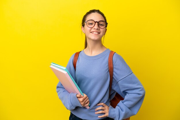 Studentka kobieta na żółtym tle pozuje z rękami na biodrach i uśmiecha się