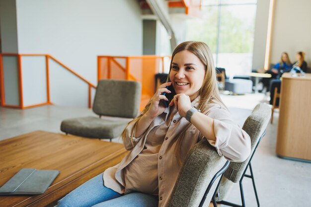 Studentka siedzi na kanapie w jasnej kawiarni z kawą i rozmawia przez telefon.