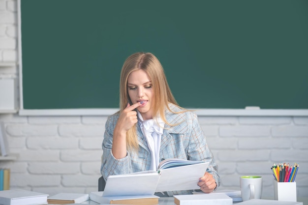 Studentka trzymająca książkę w klasie przygotowująca się do egzaminu Studentka czytająca książkę na tle tablicy z miejscem na kopię