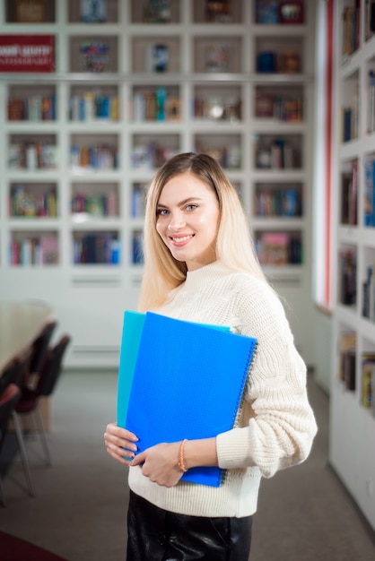 Studentka w bibliotece uniwersyteckiej, w tle półki z książkami.