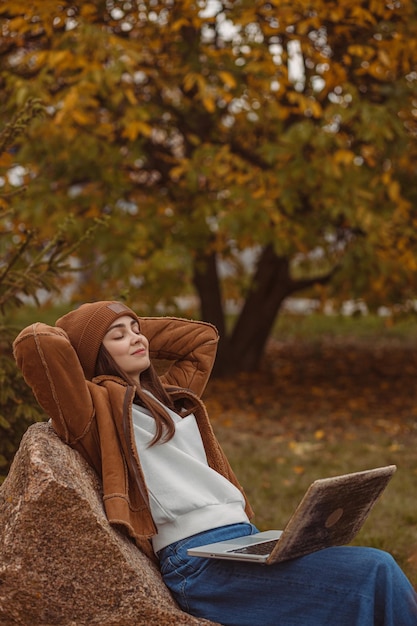 studentka w hipsterskim stroju z laptopem relaksuje się z rękami za głową na skale