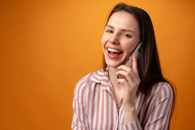 Studio fotograficzne młodej kobiety rozmawiającej przez telefon na żółtym tle