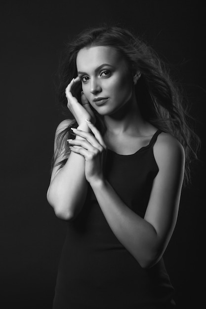 Studio mody portret kobiety glamour brunetka z idealnym makijażem i fryzurą nosi klasyczną czarną sukienkę pozowanie w ciemnym studio. Czarno-biały strzał