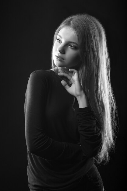 Studio monochromatyczny portret cudownej blond kobiety ubranej w czarną sukienkę pozującą w cieniu