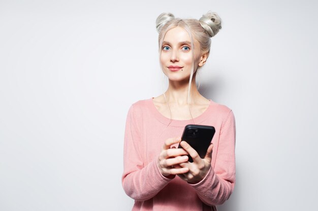 Studio portret ładnej dziewczyny z kokami do włosów, trzymając smartfon w rękach
