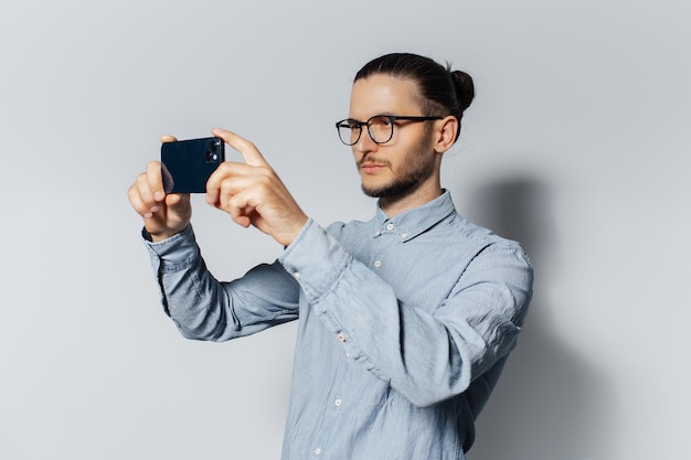 Studio portret młodego poważnego mężczyzny robi zdjęcie na smartfonie na białym tle