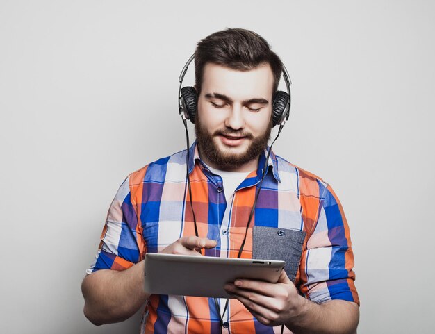 Studio portret przystojnego brodatego mężczyzny korzystającego z tabletu ze słuchawkami na jasnoszarym tle