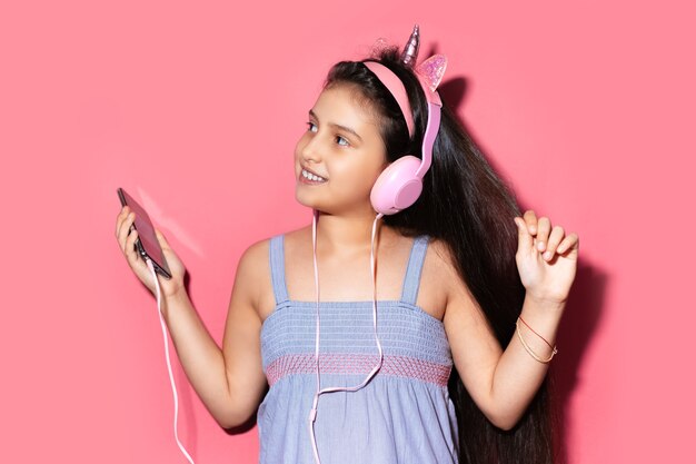 Studio portret szczęśliwe małe dziecko dziewczynka, taniec i słuchanie muzyki w słuchawkach, trzymając smartfon