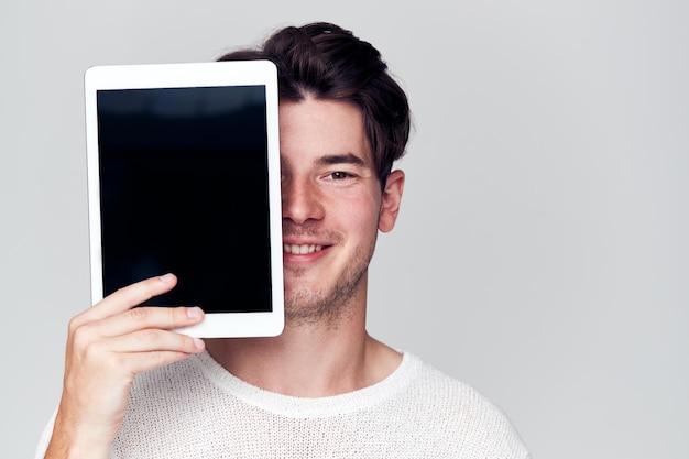 Studio portret uśmiechniętego młodego mężczyzny zakrywającego twarz cyfrowym tabletem