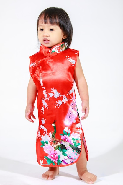Studio strzałów mały śliczny niewinny azjatycki przedszkolak córka dziewczyna dziecko model krótkie czarne włosy w czerwonym chińskim tradycyjnym stroju qipao Cheongsam stojącego samotnie na białym tle.